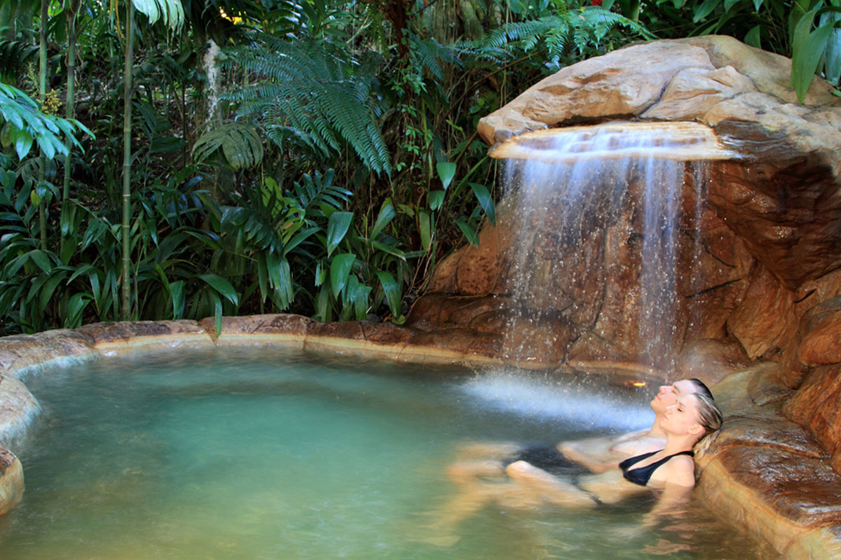 A couple relaxes with their eyes closed in a pool at The Springs Resort, with mini-waterfall feature.
