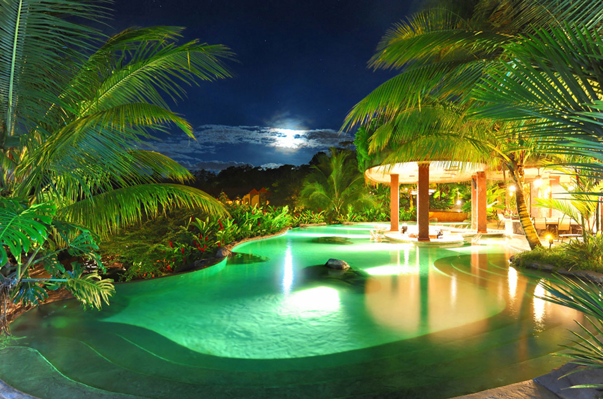 A stunning, illuminated pool at The Springs resort is surrounded by palm trees on a moonlit night.
