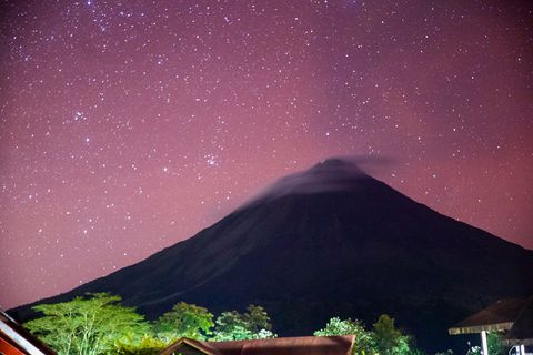 Stars glitter a
          purple sky above Arenal Volcano at night.